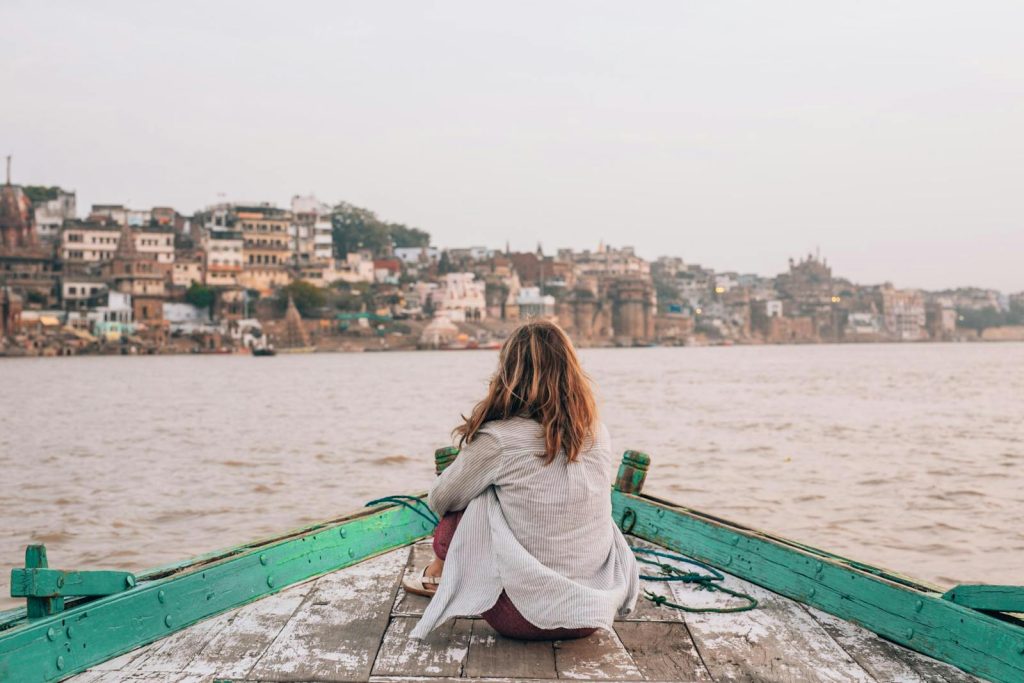 Woman sitting on a boat enjoying the tranquil view of Varanasi cityscape.